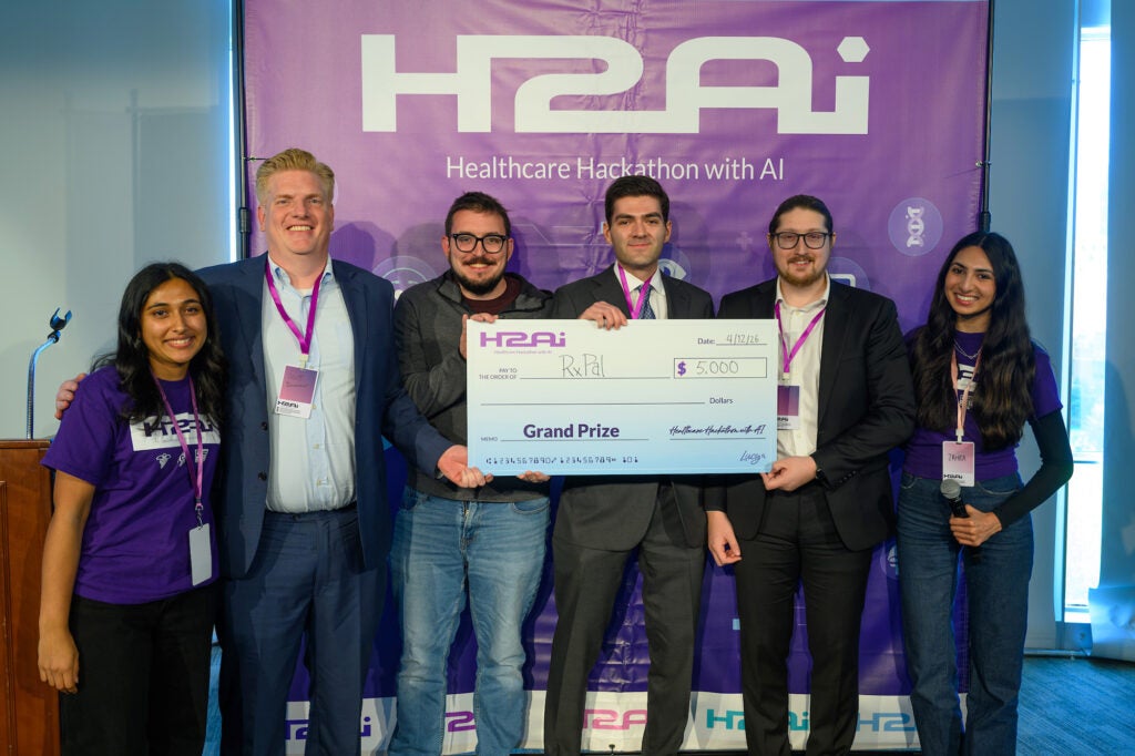 Six individuals stand together with three holding a large award