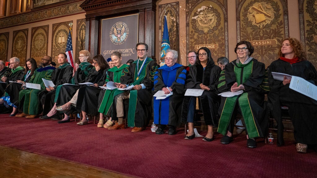 Faculty members sit in a row onstage in Gaston Hall