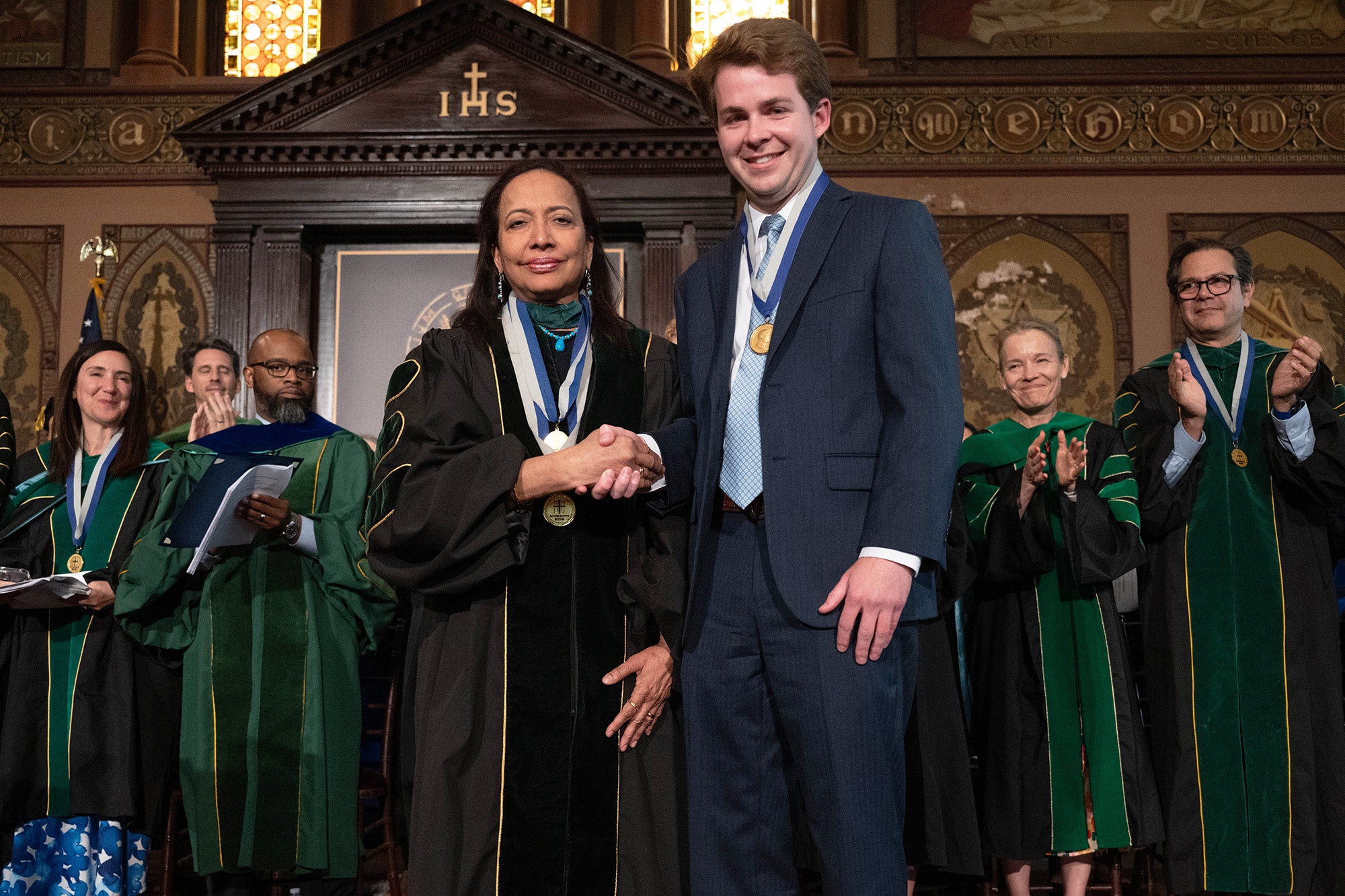 Princy Kumar shakes hands with Jack Garside while faculty applaud in the background
