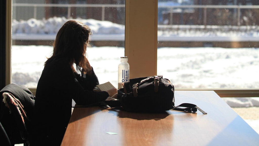 A student studies at a table by a window outside of which is snow