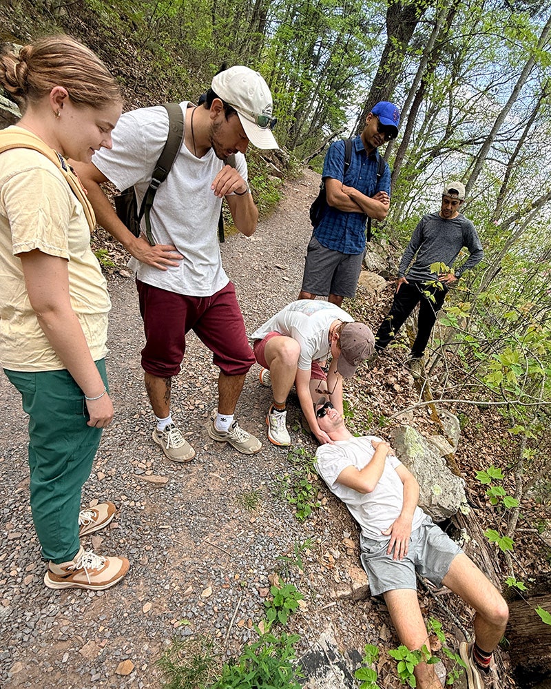 Students gather around a person lying prone on the ground holding his shoulder