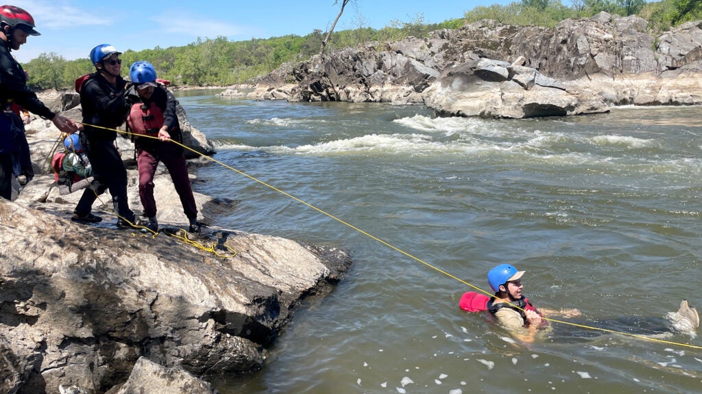 Three individuals perform a water rescue of a person floating in the river