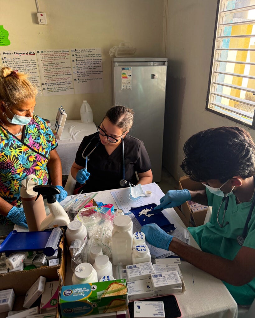 A medical student interacts with a Dominican doctor while another student counts pills