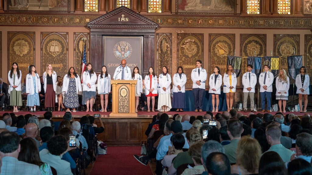 Students stand in a line onstage in Gaston Hall taking turns speaking from a podium