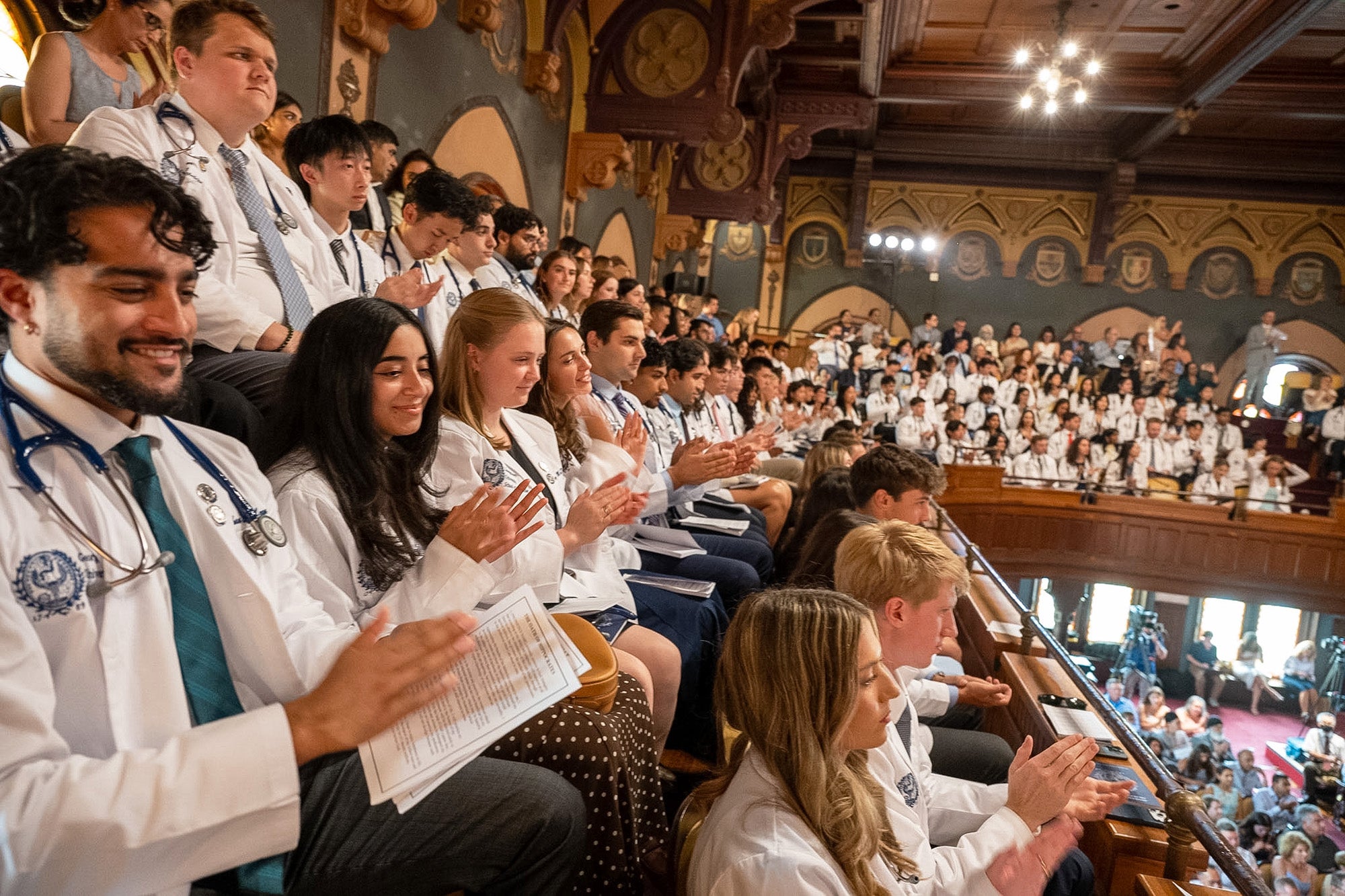 Rows of medical students wearing their white coats applaud